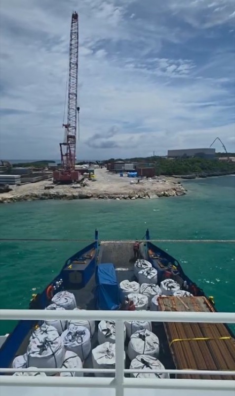 Bagged cargo on deck arriving at an island construction site with a crane on shore